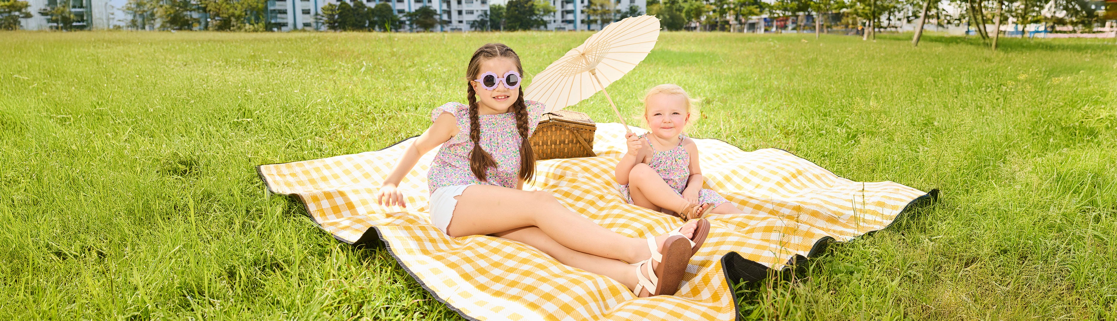 Two girls on a picnic blanket wearing liberty print clothing from ce-jour la