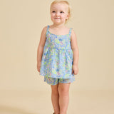 A young child standing against a beige background, wearing a floral sleeveless top and shorts with a bow on the back.