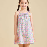 A young girl standing against a beige background, wearing the ce-jour la fleur sleeveless knee-length dress with adjustable shoulder straps.