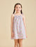 A young girl standing against a beige background, wearing the ce-jour la fleur sleeveless knee-length dress with adjustable shoulder straps.