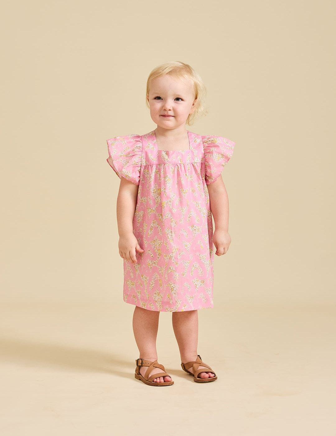 A toddler in a pink floral dress with short, fluttered sleeves and knee-length.