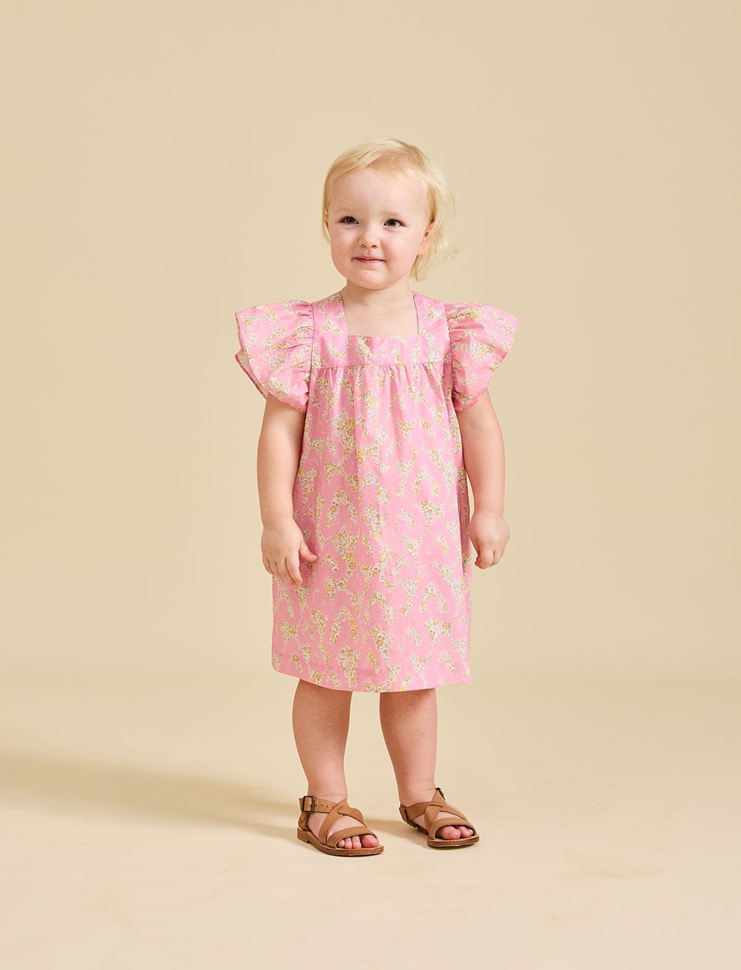 A toddler in a pink floral dress with short, fluttered sleeves and knee-length.