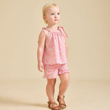 A child standing wearing a pink floral top and matching shorts with tan sandals.